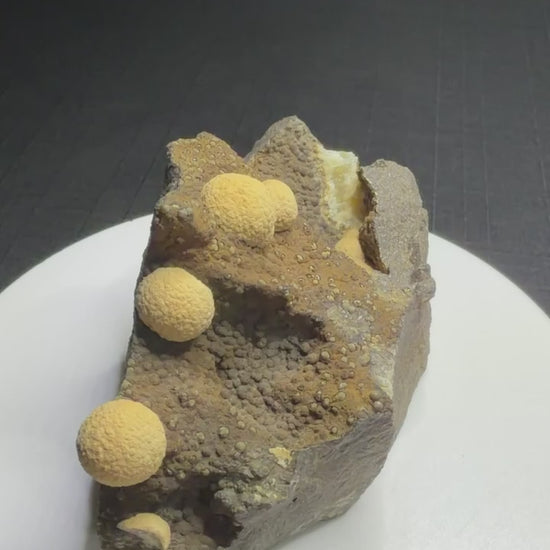 Pale yellow spherical calcite formations on dark basalt from Zhejiang Province, China