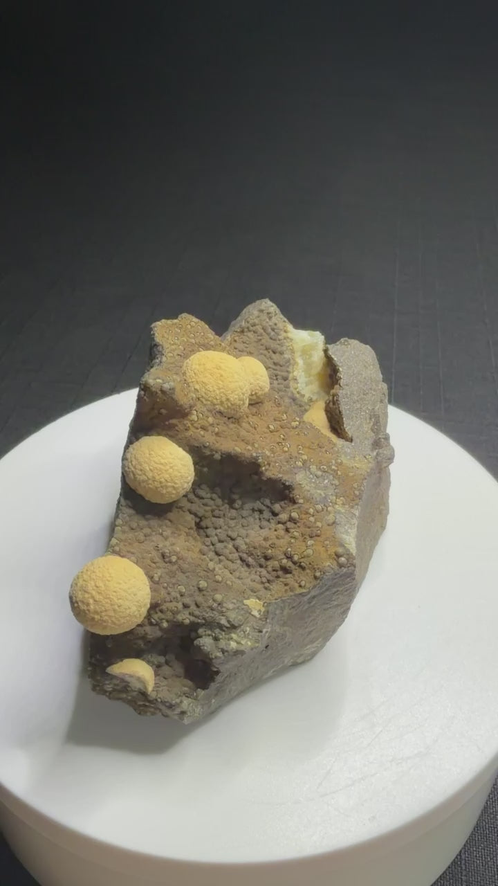 Pale yellow spherical calcite formations on dark basalt from Zhejiang Province, China