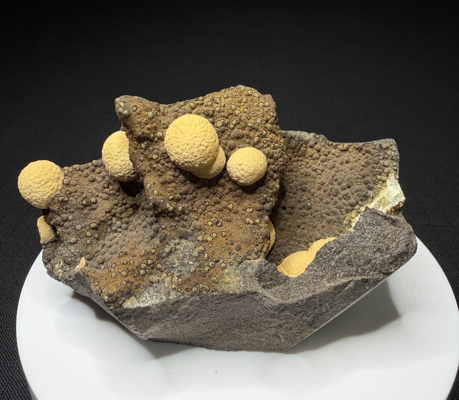 Pale yellow spherical calcite formations on dark basalt from Zhejiang Province, China