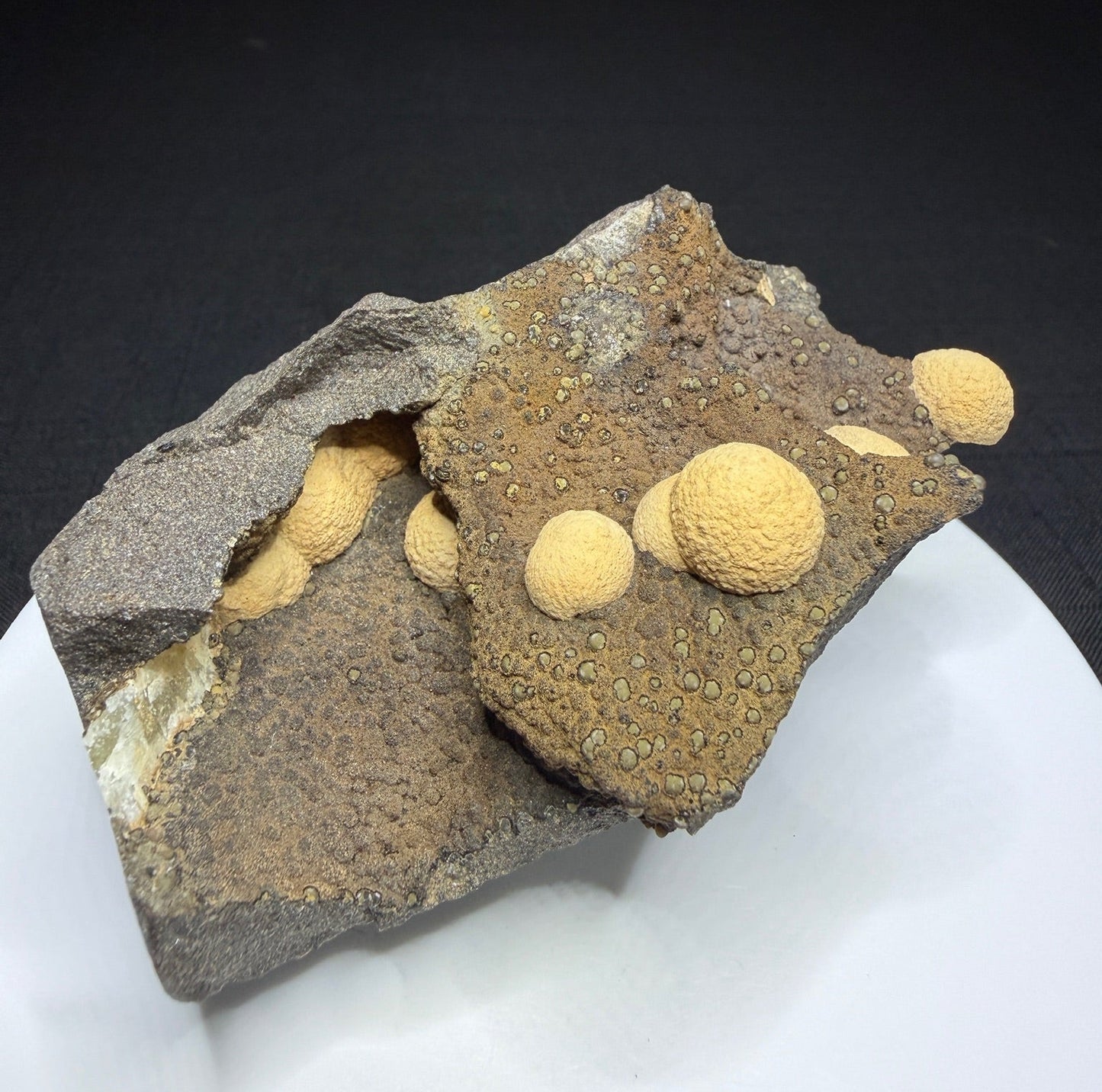 Pale yellow spherical calcite formations on dark basalt from Zhejiang Province, China